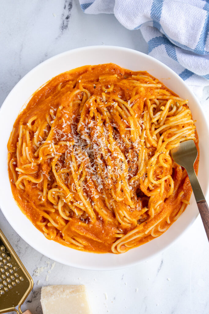 Overhead view of a white pasta bowl filled with spaghetti covered in butternut squash pasta sauce topped with parmesan cheese.