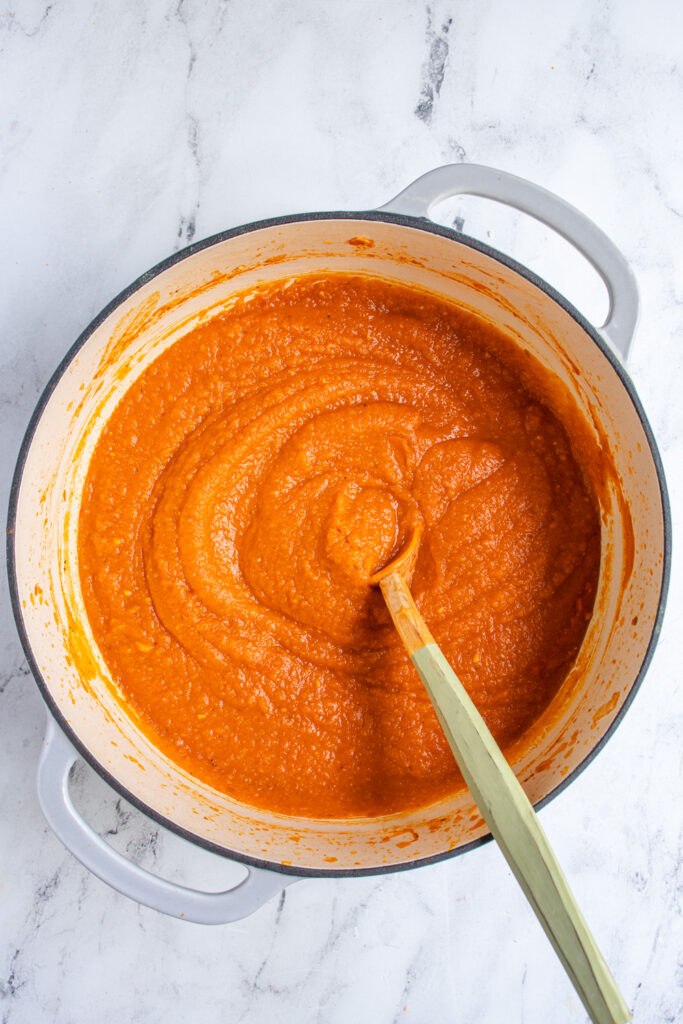 A large gray pot filled with butternut squash pasta sauce with a wooden spoon.