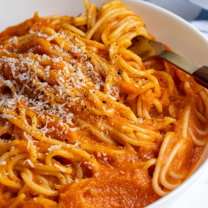 A white pasta bowl filled with spaghetti covered in butternut squash pasta sauce.