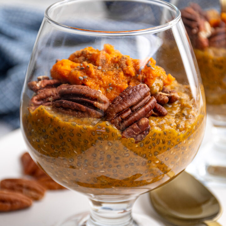 Close up of a clear glass with pumpkin chia seed pudding topped with pecans and pumpkin puree.