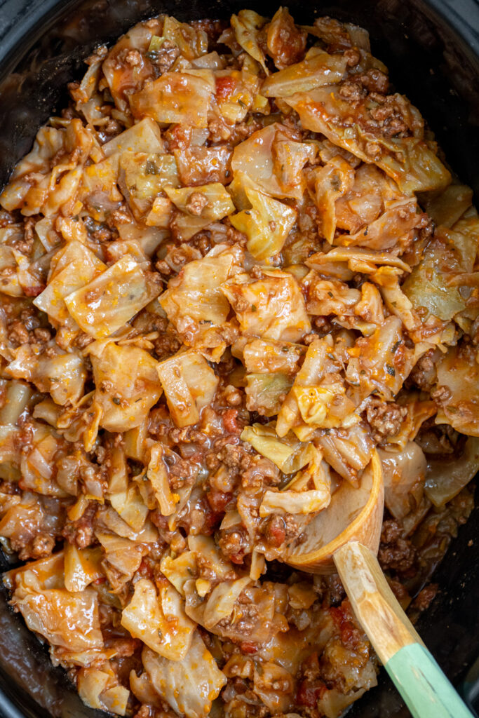 A wooden spoon in a slow cooker full of lazy cabbage rolls.
