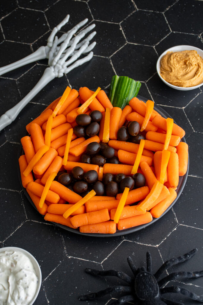A veggie platter arranged to look like a jack'o lantern pumpkin with carrots and olives.