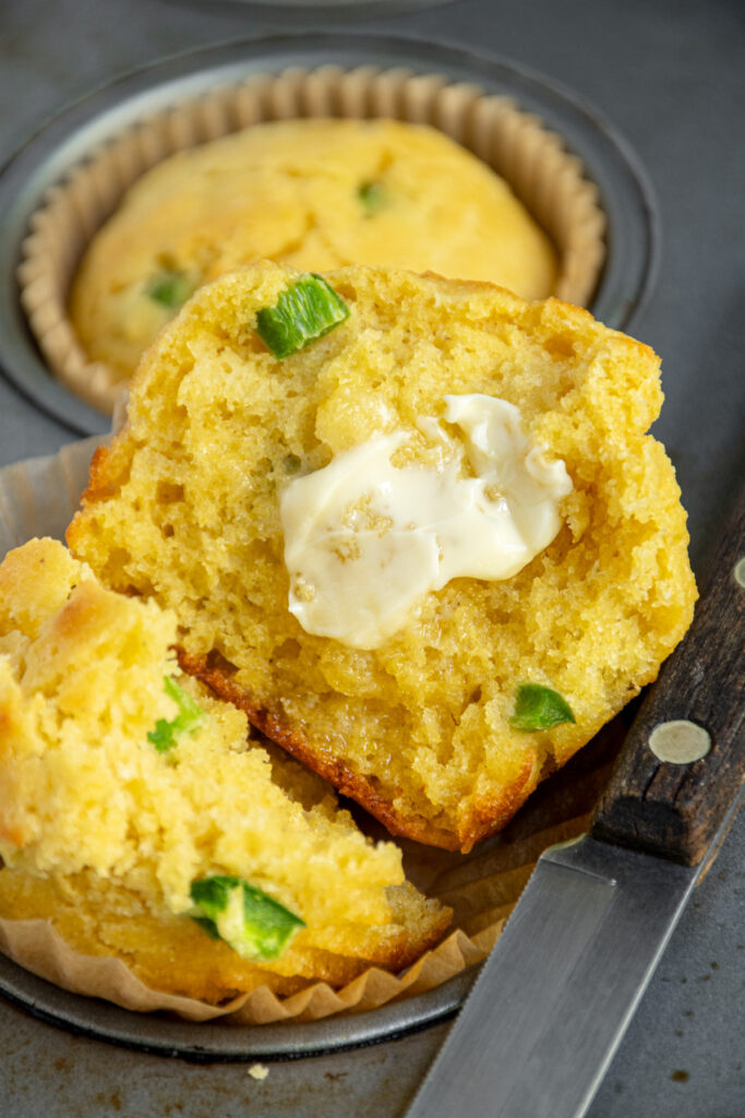 Close up of a jalapeño cornbread muffin opened in half to reveal a moist crumbly inside with a smear of soft butter.