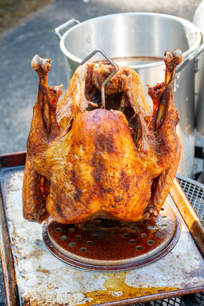 A freshly deep fried turkey on a stand with the deep fryer in the background.
