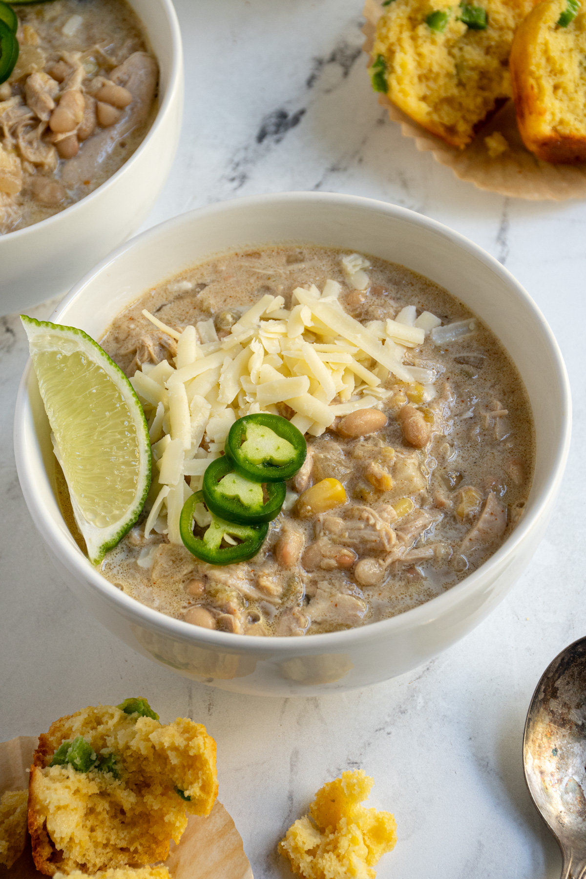 A white bowl filled with crockpot white chicken chili garnished with sharp cheddar, jalapeños, and lime wedge.