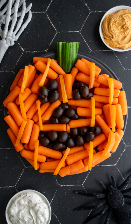 A halloween veggie tray idea made to look like a pumpkin with carrots, cucumber, and black olives.