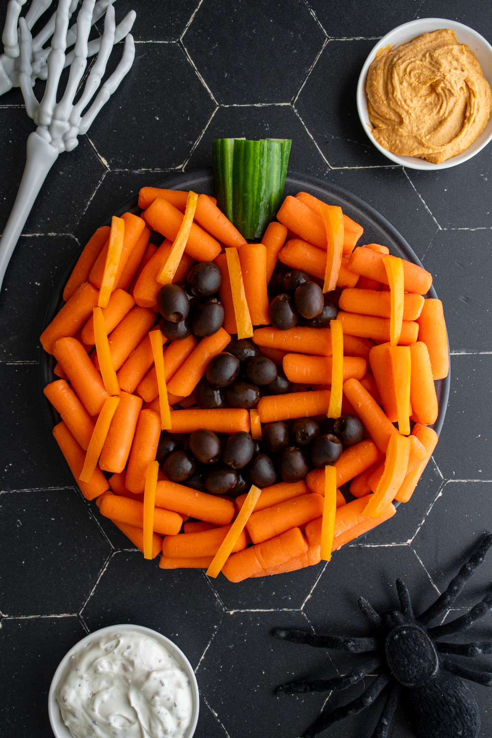 A halloween veggie tray idea made to look like a pumpkin with carrots, cucumber, and black olives.