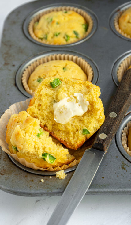 A jalapeño cornbread muffin opened in half to reveal a moist and tender crumb with a smear of butter.