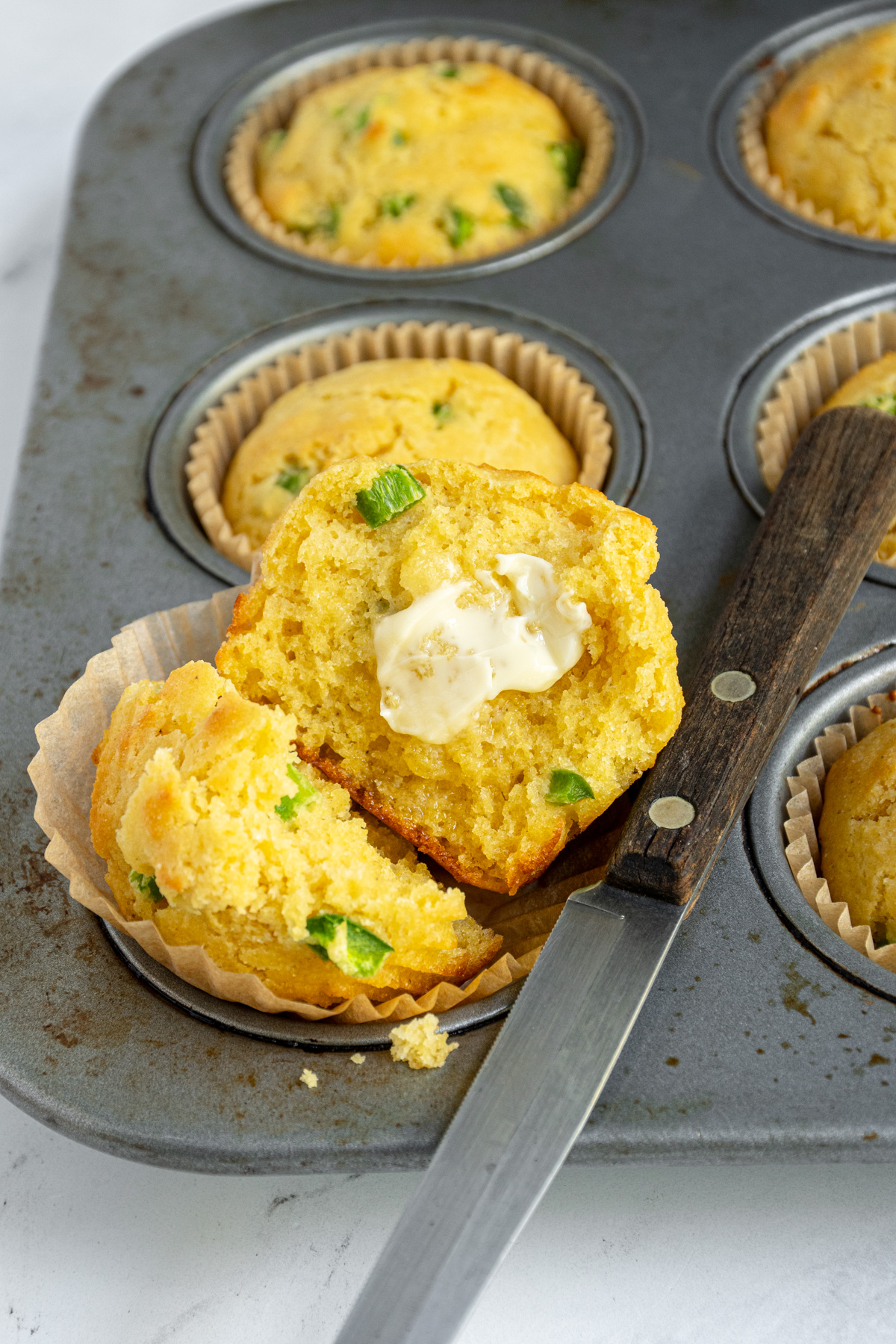 A jalapeño cornbread muffin opened in half to reveal a moist and tender crumb with a smear of butter.