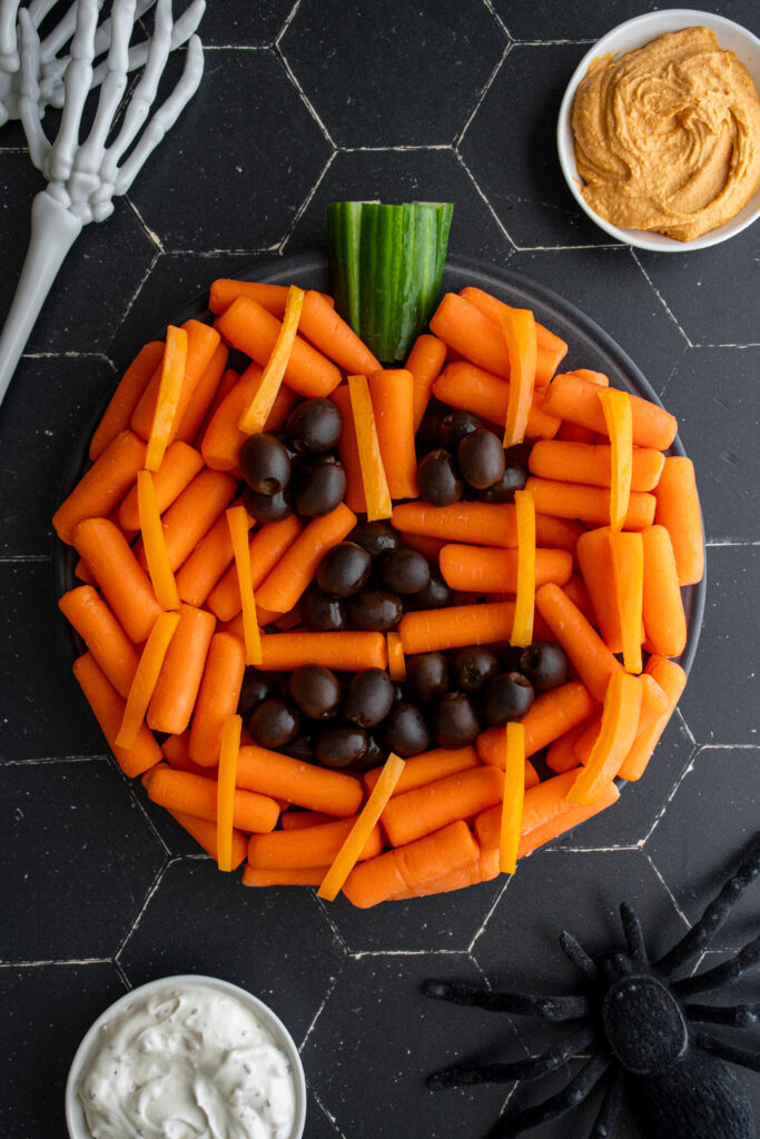 A Jack'O Lantern Pumpkin Veggie tray with carrots and black olives.
