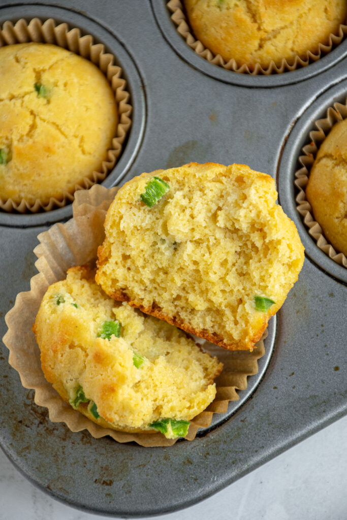 A jalapeño cornbread muffin cut in half releasing a tender crumb on the inside with speaks of diced jalapeño.