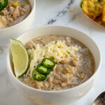 Pinterest pin with text overlay "Crockpot White Chicken Chili", image of a white bowl filled with white chicken chili garnished with sharp white cheddar.