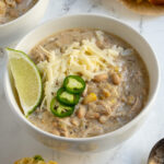 Pinterest pin with text overlay "Crockpot White Chicken Chili", image of a white bowl filled with white chicken chili garnished with sharp white cheddar.