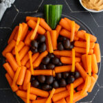 Pinterest pin with text overlay "Easy Halloween Veggie Tray", image of a pumpkin veggie tray made with baby carrots and olives.