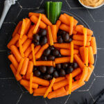 Pinterest pin with text overlay "Easy Halloween Veggie Tray", image of a pumpkin veggie tray made with baby carrots and olives.