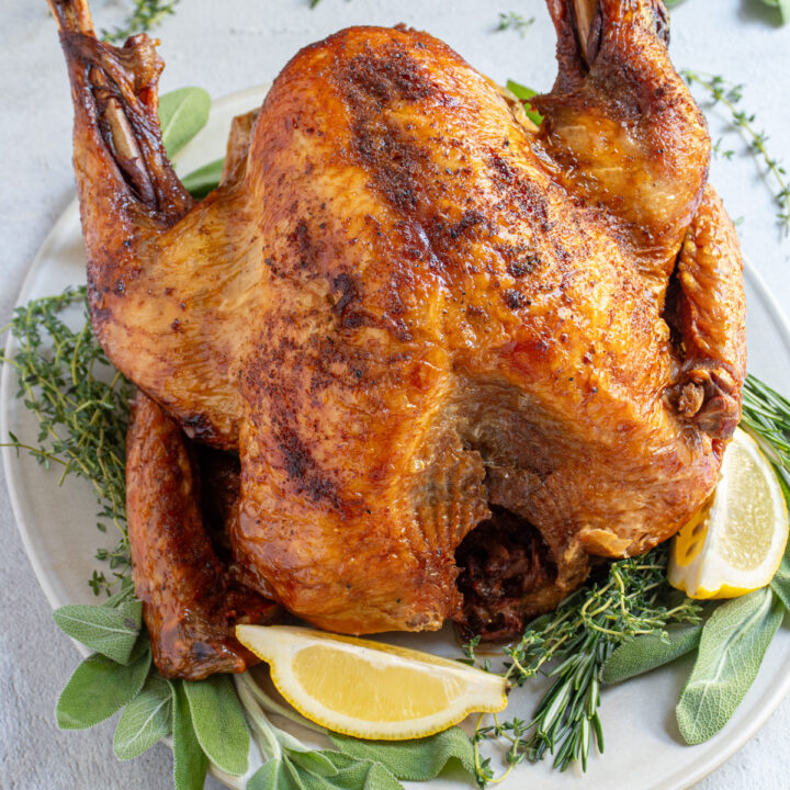 A platter with herbs sits a golden brown best deep fried turkey ready to be carved.