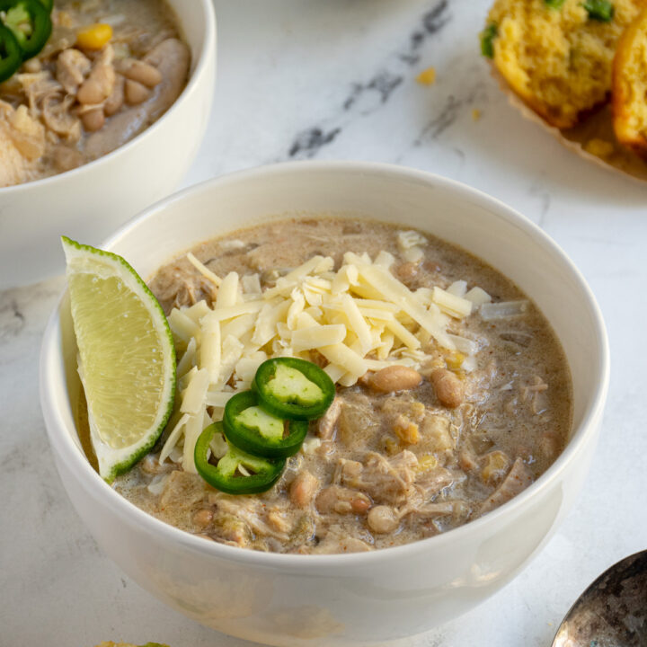 White bowl filled with slow cooker white chicken chili garnished with white sharp cheddar cheese.