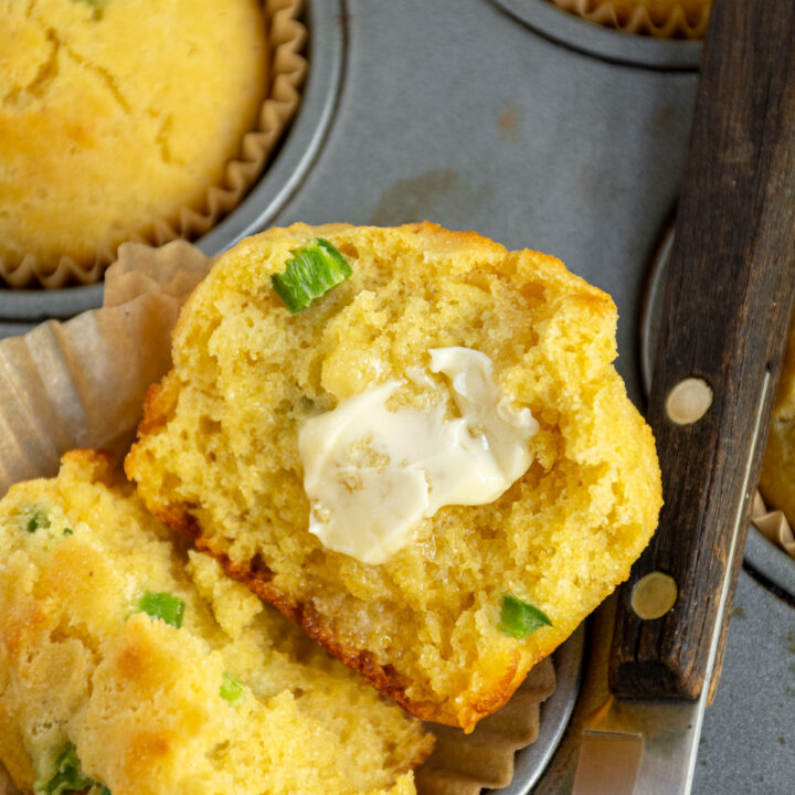 A cut in half jalapeño cornbread muffin with a smear of butter laid out in the muffin wrapper.