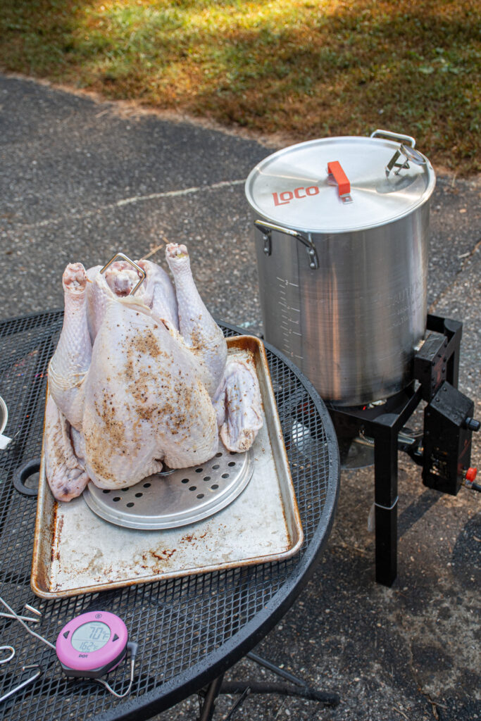 A set up of a table with a raw turkey on a stand with a meat thermometer sitting next to a deep fryer.