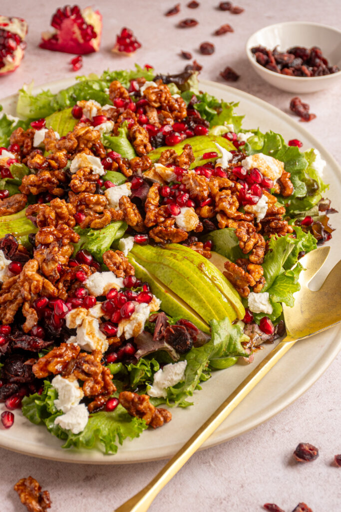 A large platter with a big winter salad with candied walnuts, pears, pomegranate seeds, cranberries, and goat cheese.