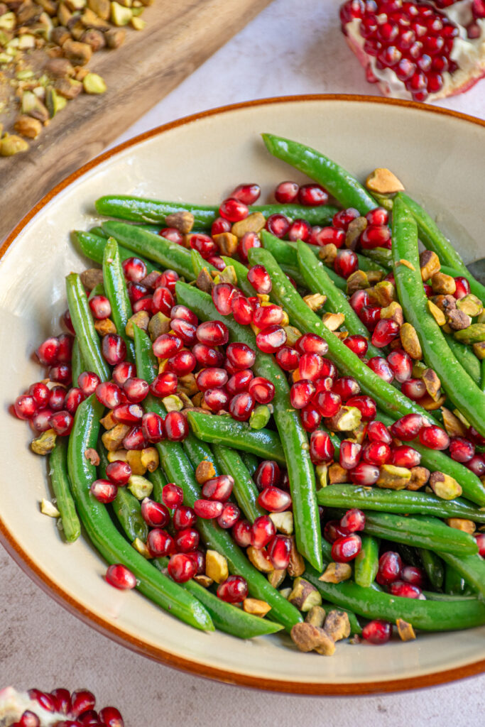 A serving bowl with sautéed green beans topped with pomegranate seeds and pistachios.