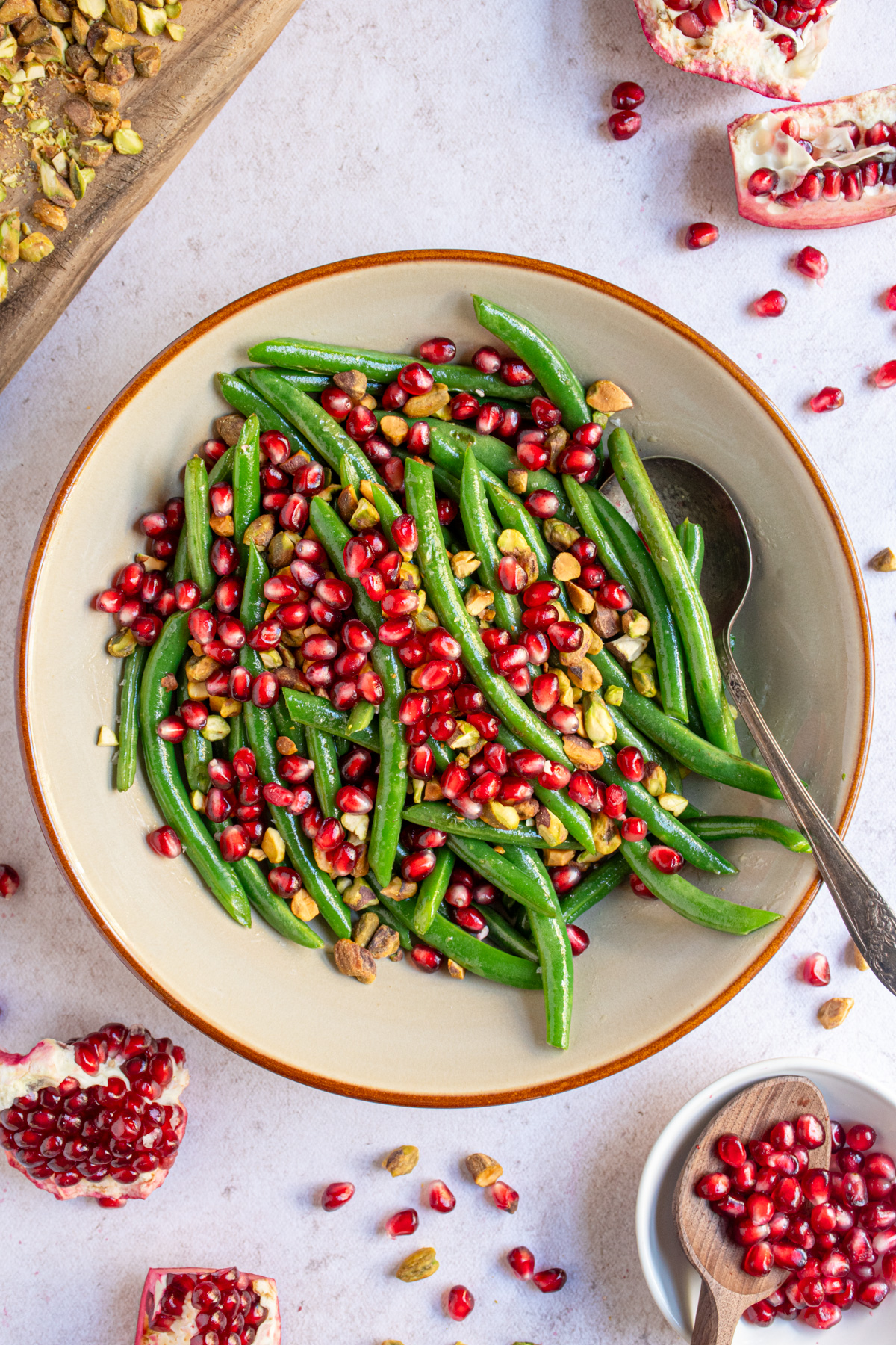 A brown serving bowl filled with bight green beans and topped with red pomegranate seeds and chopped pistachios.