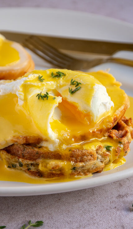 An opened poached egg with runny yolk on top of a thanksgiving eggs benedict with a stuffing waffle and turkey.