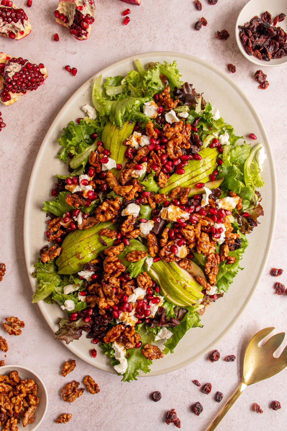 A large platter covered in a festive winter salad with candied walnuts, pomegranates, dried cranberries, pears, and goat cheese.