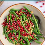 Pinterest pin with text overlay "Green Beans with Pomegranate & Pistachios", image of a bowl of bright green beans with red pomegranate seeds and pistachios.