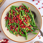 Pinterest pin with image of a bowl of bright green beans with red pomegranate seeds and pistachios.