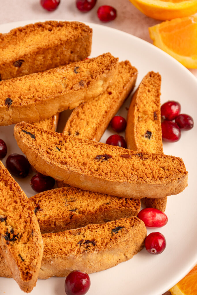 A piece of Orange Cranberry Biscotti sitting on top of a pile of biscotti on a plate.