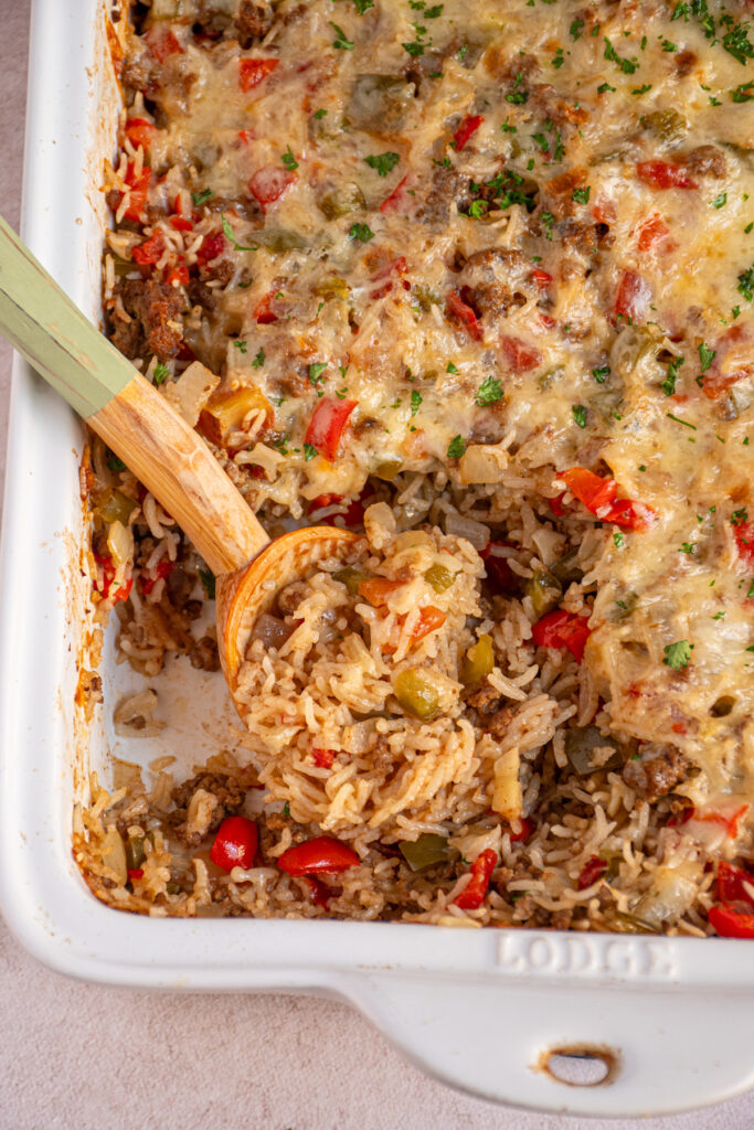 A white dish filled with stuffed pepper casserole with a wooden spoon showing rice, beef, and peppers.