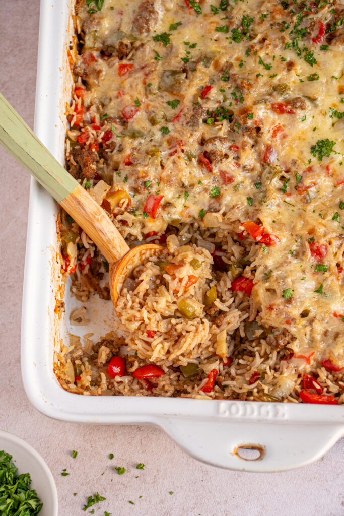 Stuffed Pepper Casserole in a white baking dish with a wooden spoon that has scooped some out showing cooked rice, ground beef, and bell peppers.