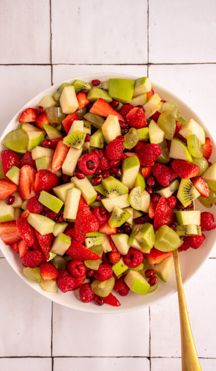 A white serving bowl filled with red and green fruits to make Christmas fruit salad.