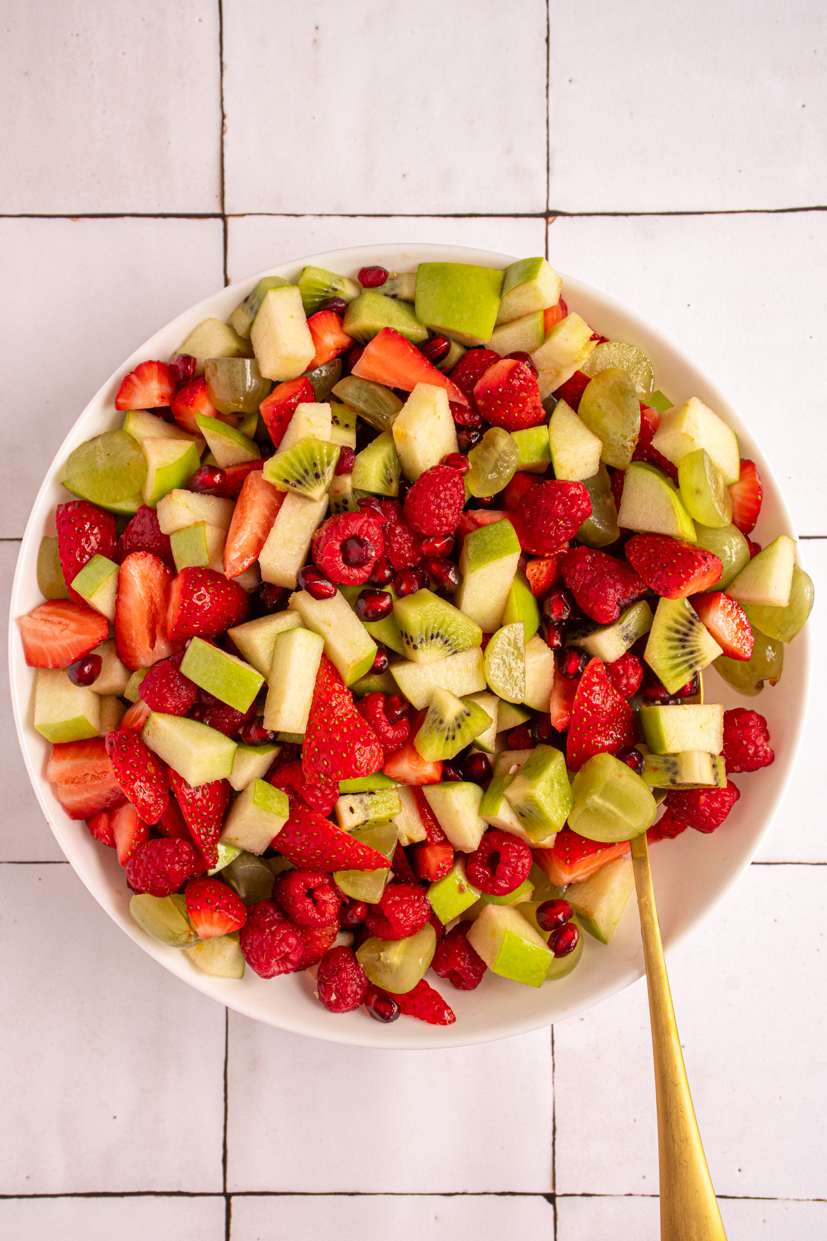 A white serving bowl filled with red and green fruits to make Christmas fruit salad.
