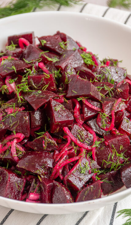 A white serving bowl with simple beet salad garnished with fresh dill.