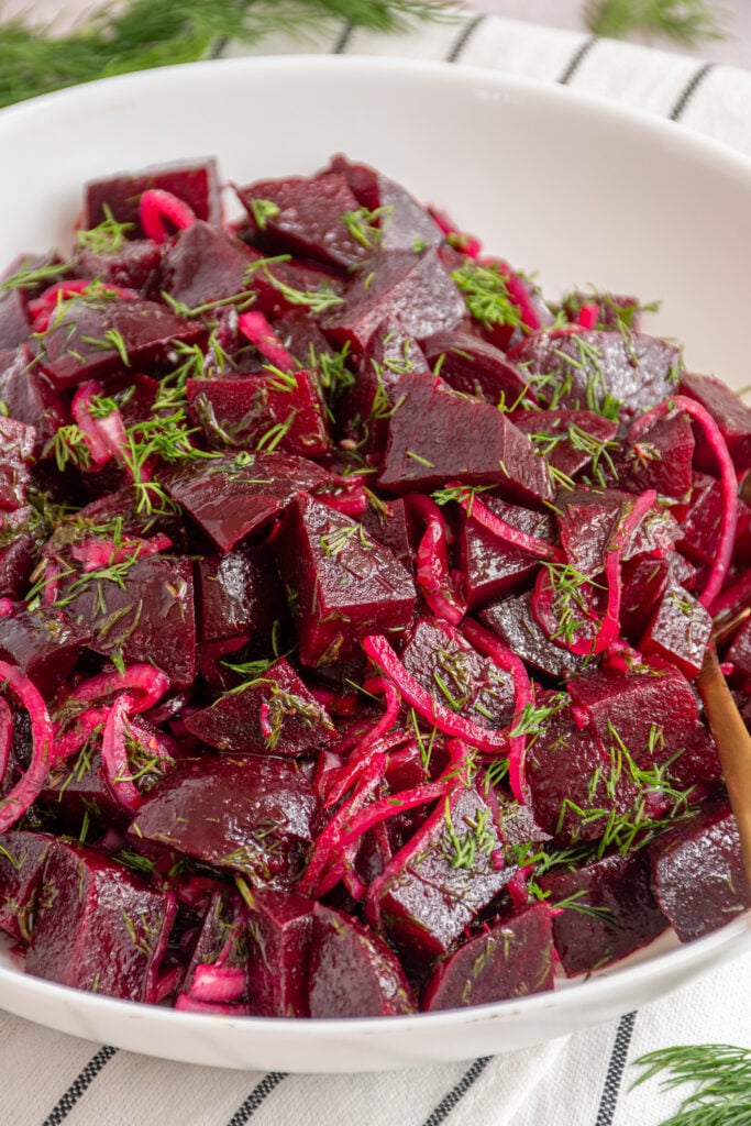 A white serving bowl with simple beet salad garnished with fresh dill.