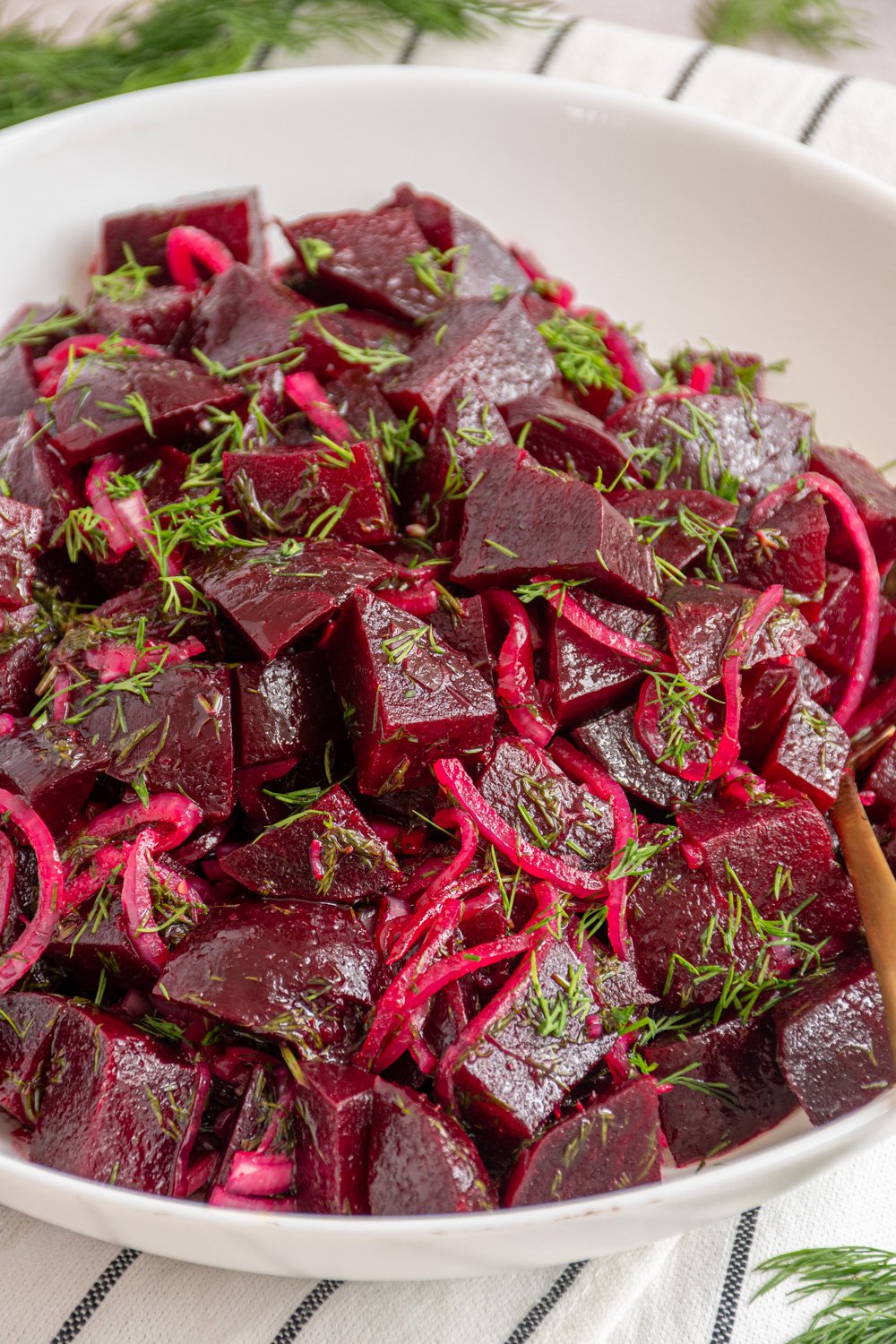 A white serving bowl with simple beet salad garnished with fresh dill.