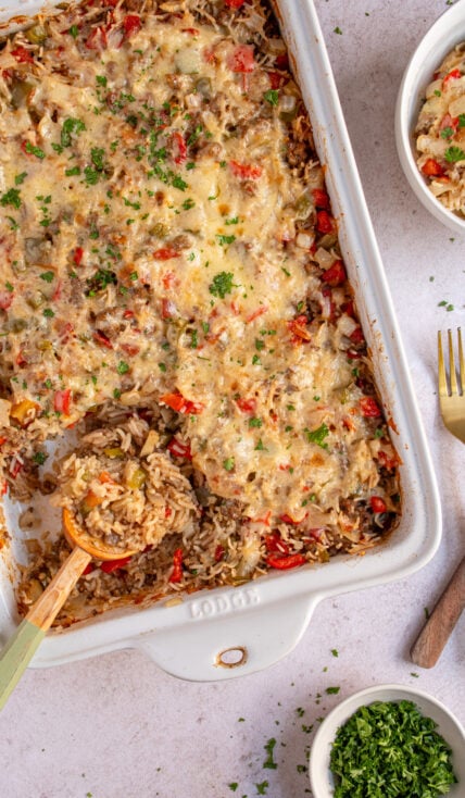 Overhead view of a white baking dish filled with stuffed pepper casserole with a wooden spoon showing a scoop filled with cooked rice, ground beef, and bell peppers.