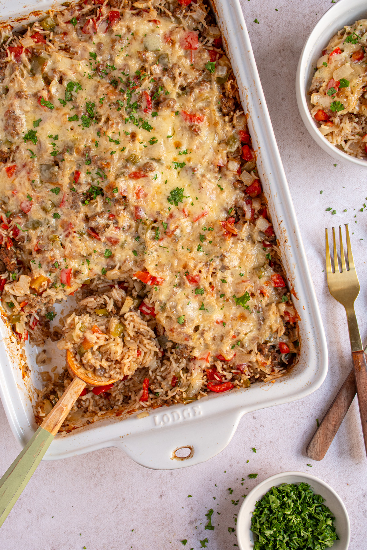 Overhead view of a white baking dish filled with stuffed pepper casserole with a wooden spoon showing a scoop filled with cooked rice, ground beef, and bell peppers.