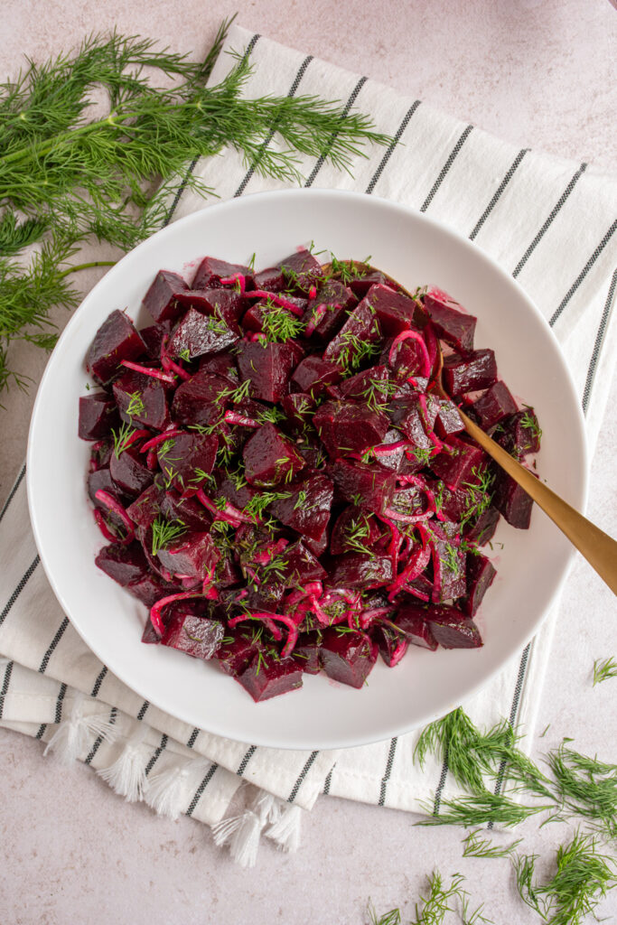 Overhead of a white serving bowl filled with simple beet salad topped with dill.