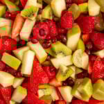 Pinterest pin with test overlay 'Christmas Fruit Salad", image of a white serving bowl filled with red and green fruits.