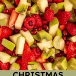 Pinterest pin with test overlay 'Christmas Fruit Salad", image of a white serving bowl filled with red and green fruits.