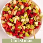 Pinterest pin with test overlay 'Christmas Fruit Salad", image of a white serving bowl filled with red and green fruits.