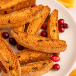 Pinterest pin with text overlay "Orange Cranberry Biscotti', image of a white plate piled with biscotti.