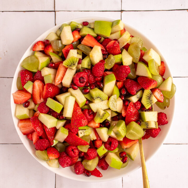Overhead of a bowl filled with red and green fruits to make Christmas fruit salad.