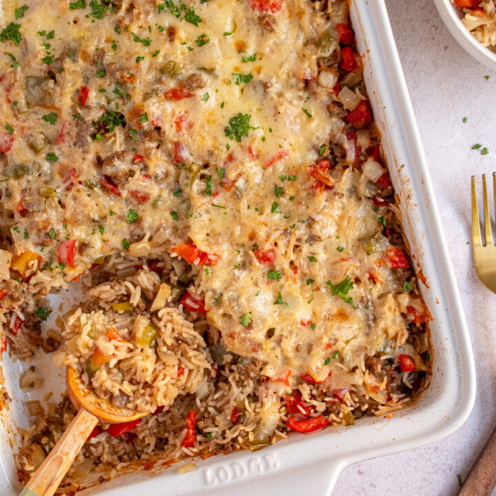 A white dish with stuffed pepper casserole with a wooden spoon scooping the casserole.