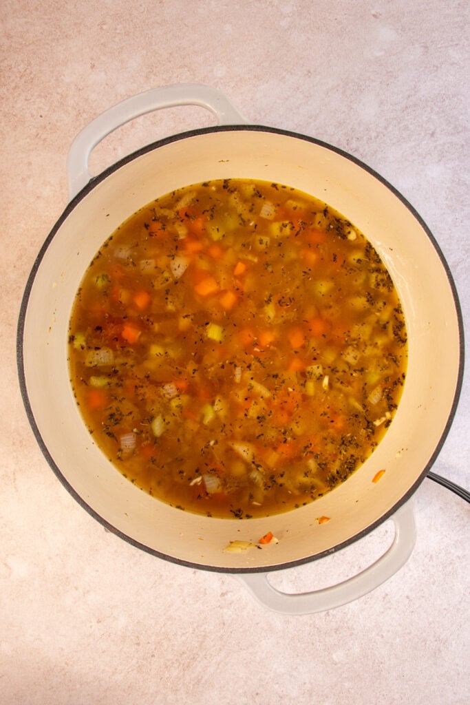 A large dutch oven with chickpeas and veggie broth being added to the soup.