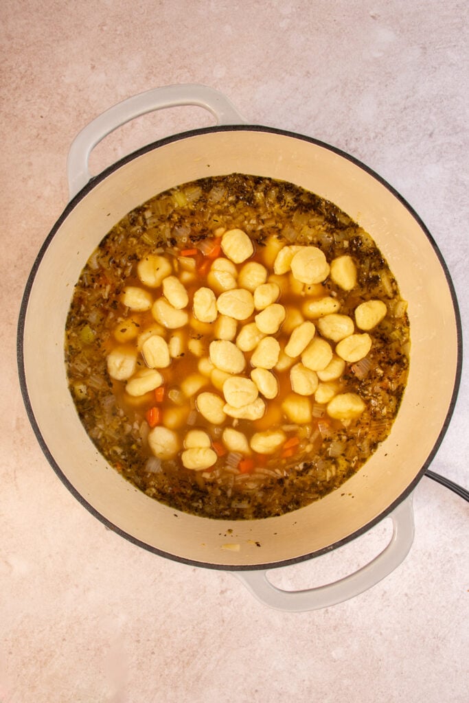 A large dutch oven in which potato gnocchi is being added to the soup.