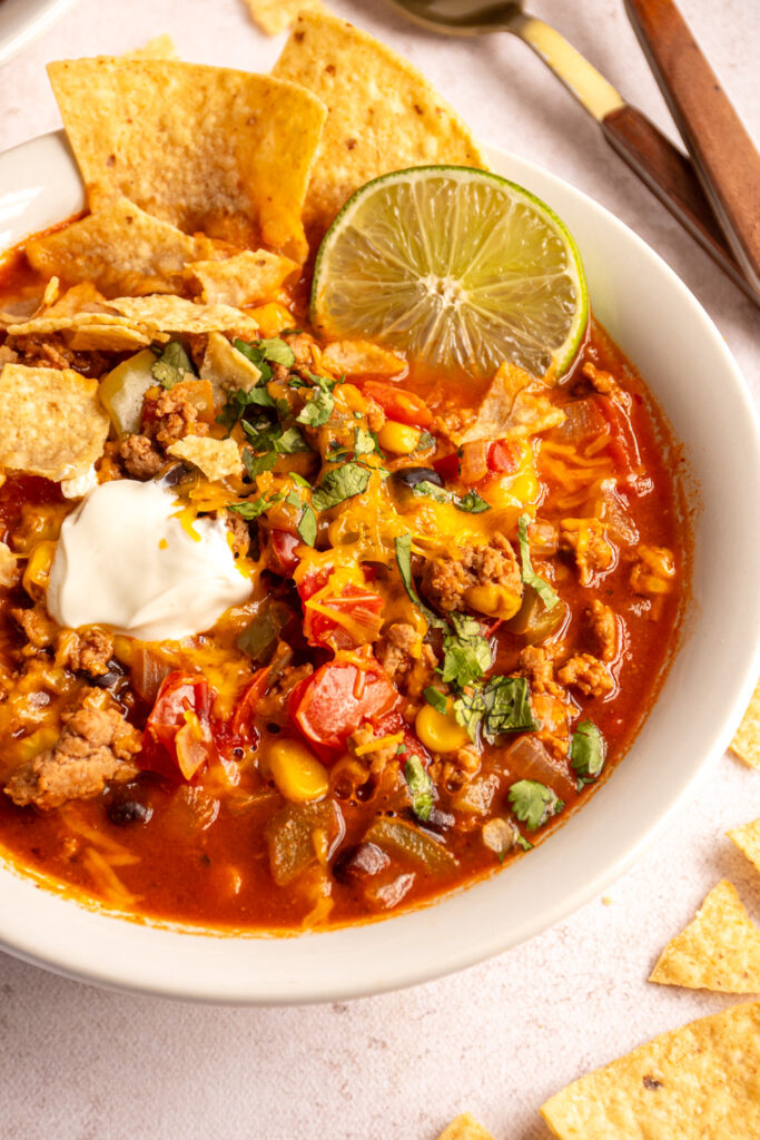 A bowl of ground tureky taco soup garnished with cheese, sour cream, cilantro, and tortilla chips.